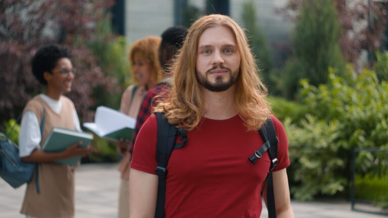Happy Caucasian student guy man male schoolboy in city outdoors university college campus showing